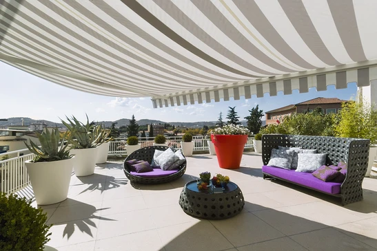 Terrasse moderne avec mobilier d'ext&eacute;rieur haut de gamme sous store banne ray&eacute;